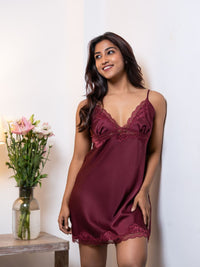 Woman wearing a burgundy lace nightgown with a vase of flowers on a table in the background.