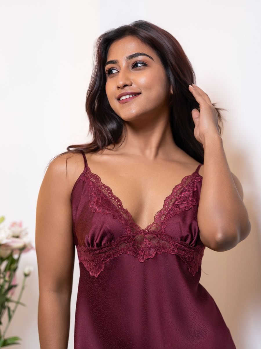 Woman wearing a burgundy lace nightgown against a neutral background