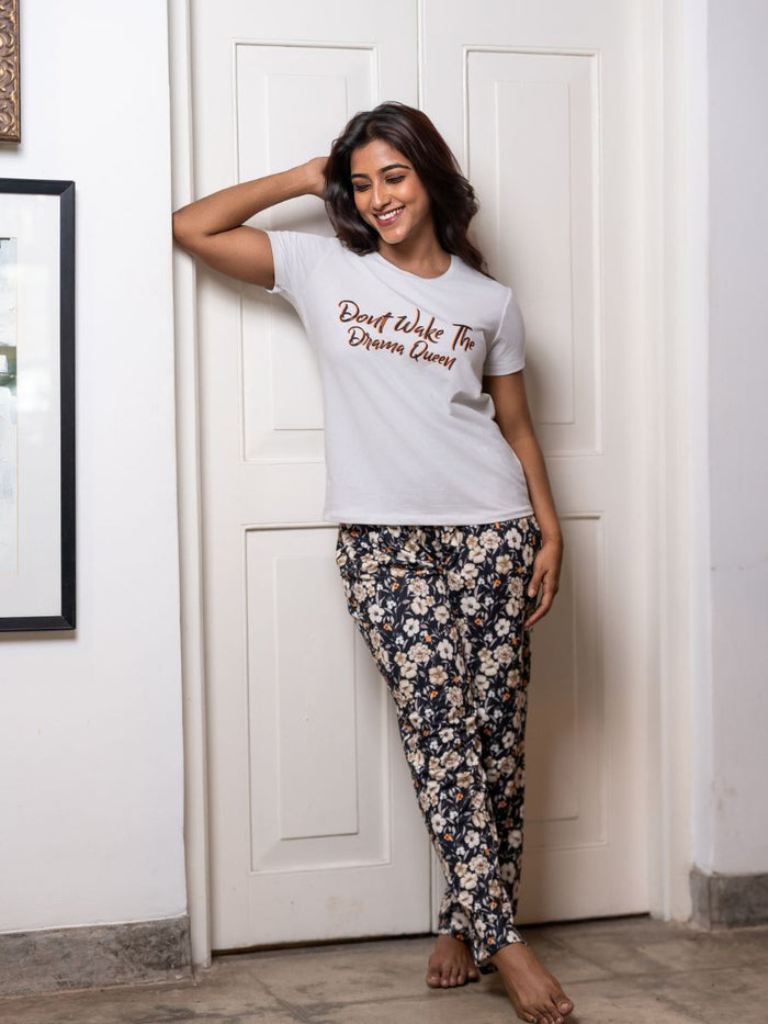Woman wearing a white t-shirt with text and floral pants standing against a white door.