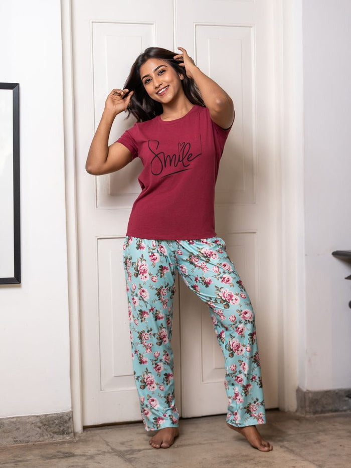 Woman wearing a red t-shirt with 'Smile' and floral pants in a room.