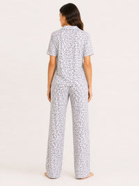 Woman wearing a white pajama set with black pattern on a light pink background