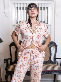 Woman wearing a floral pajama set in a room with chairs and a lamp.