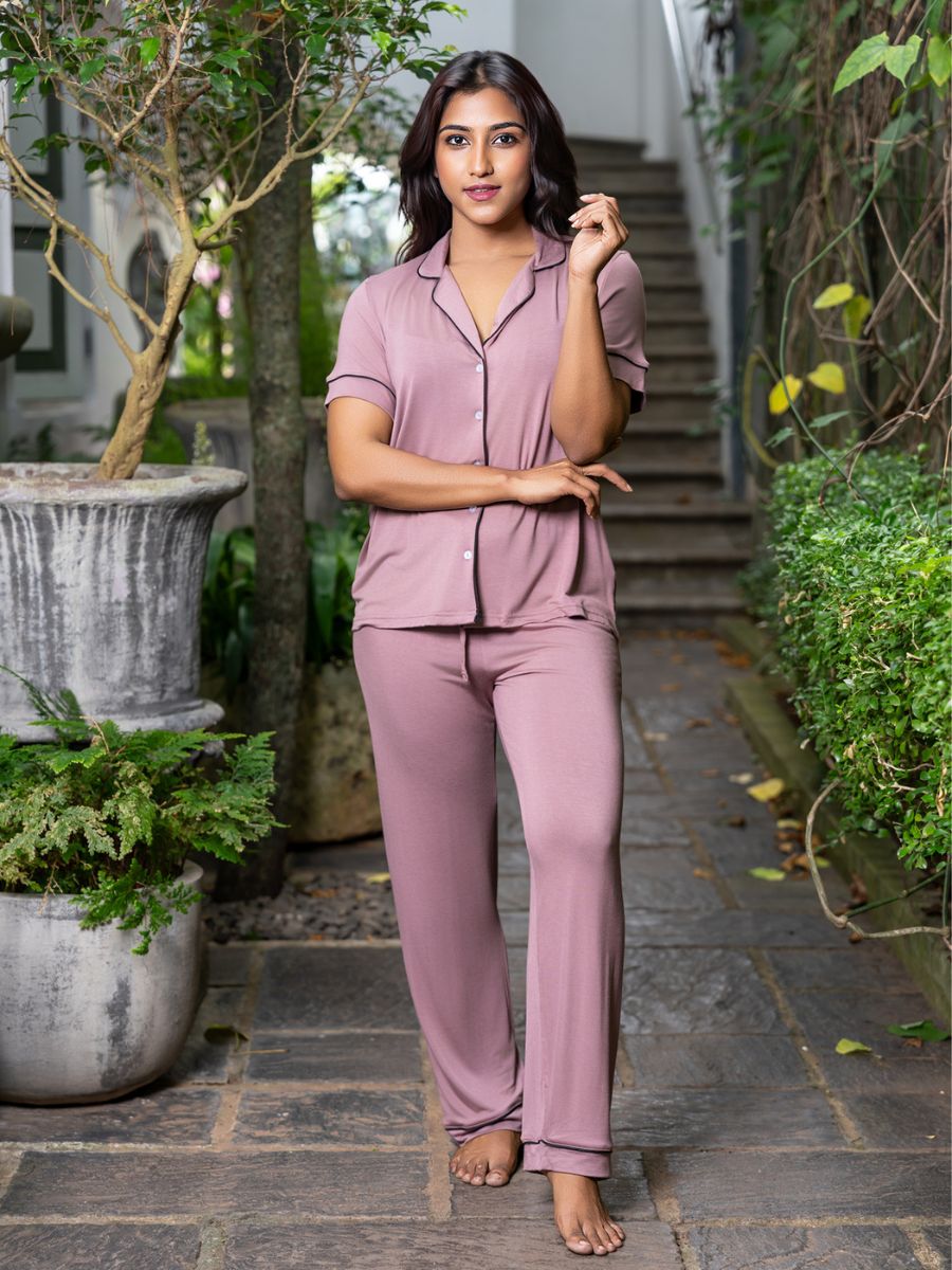 Woman wearing a pink pajama set standing outdoors with plants and steps in the background