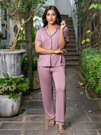 Woman wearing a pink pajama set standing outdoors with plants and steps in the background