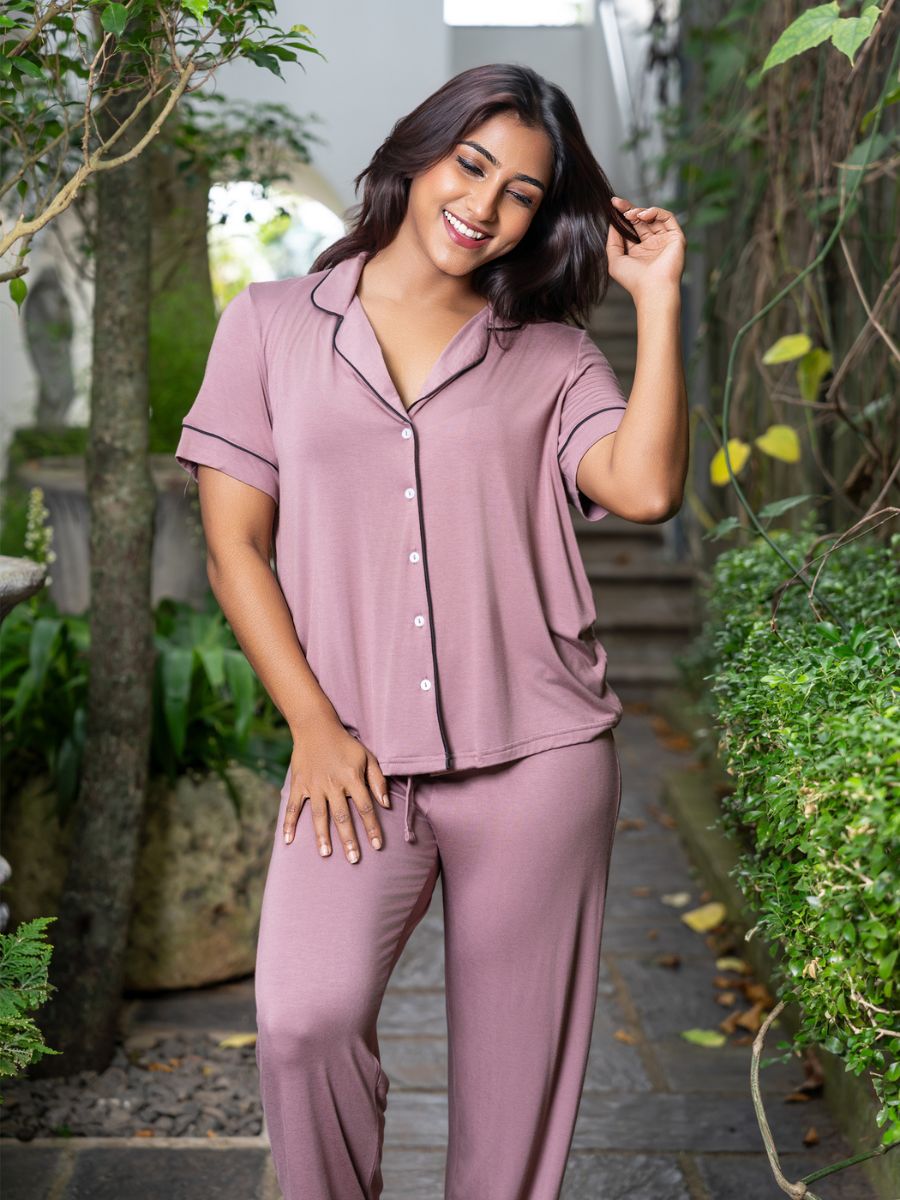 Woman wearing a mauve pajama set outdoors with greenery.