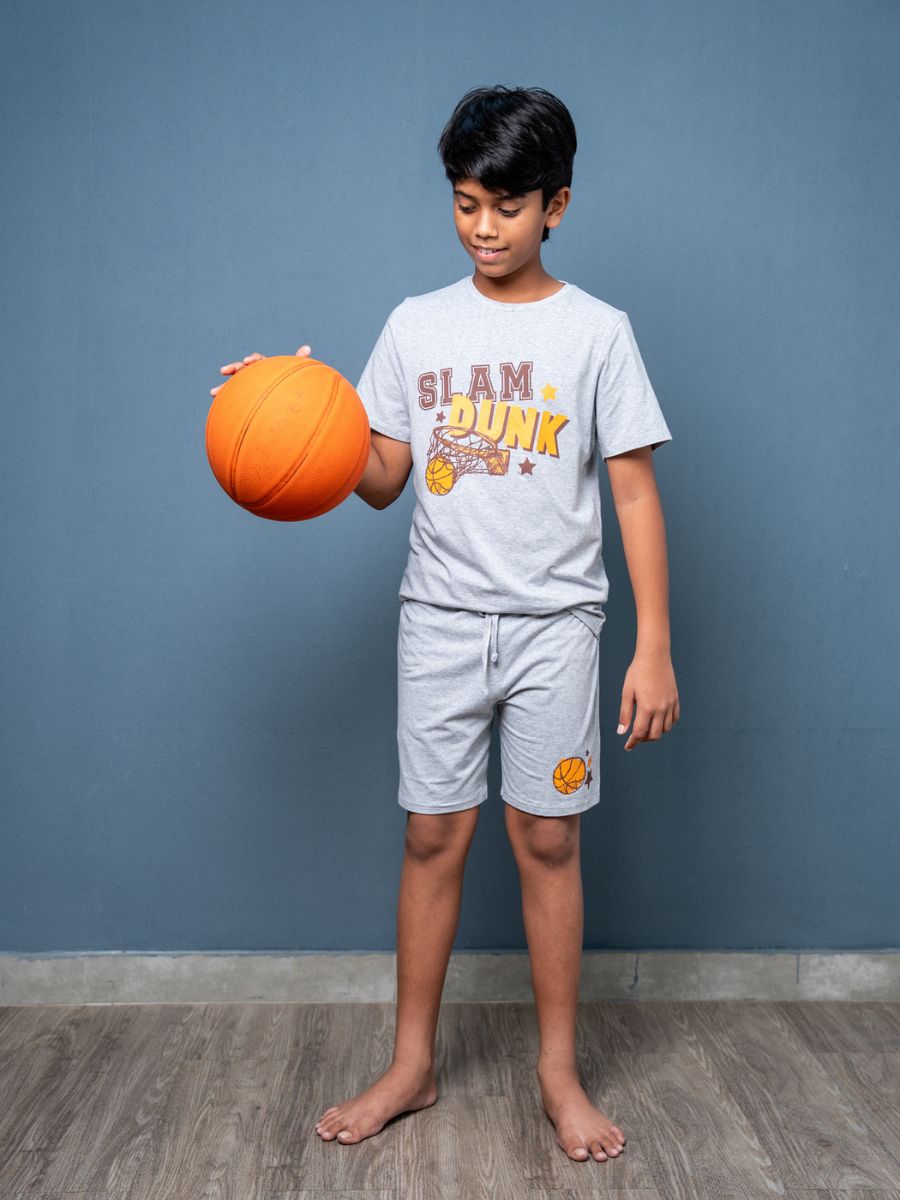 Child holding an orange basketball wearing a 'Slam Dunk' t-shirt against a blue wall.