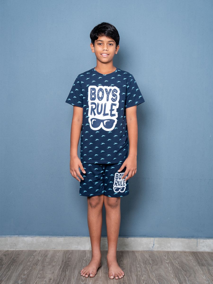 Child wearing a navy blue pajama set with 'Boys Rule' text against a blue wall.