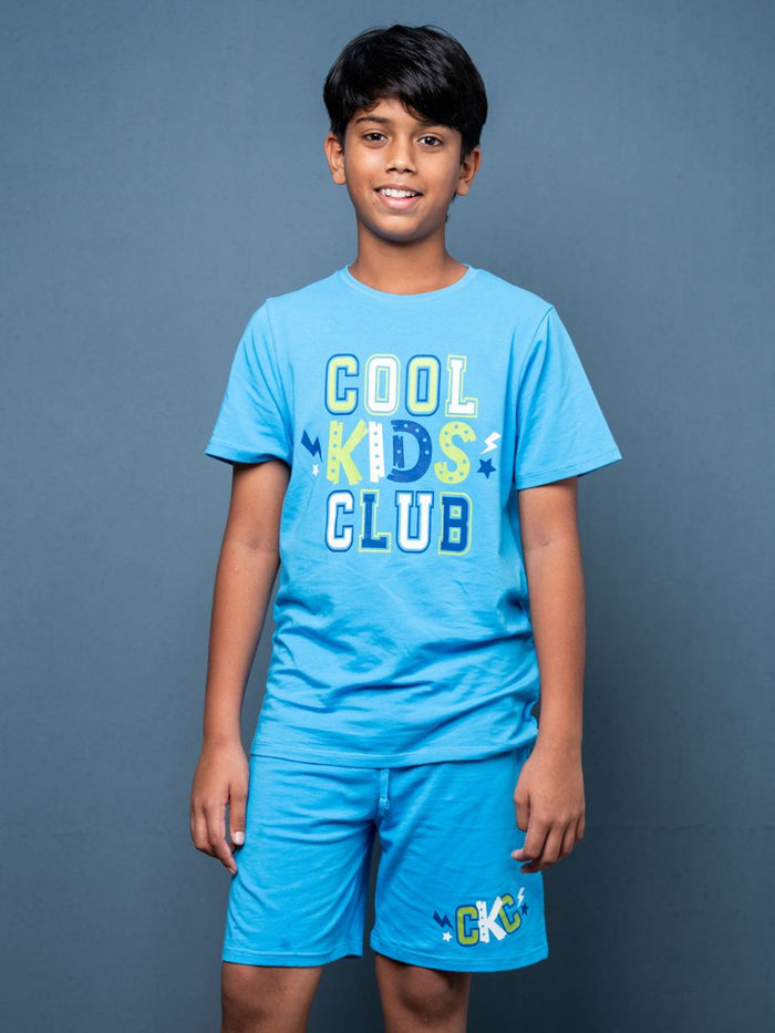 Child wearing a blue 'Cool Kids Club' t-shirt and shorts on a gray background