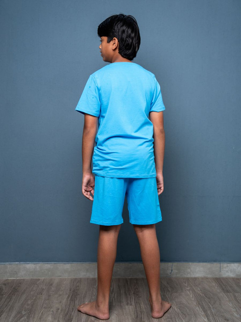 Child wearing a blue t-shirt and shorts set against a gray wall.