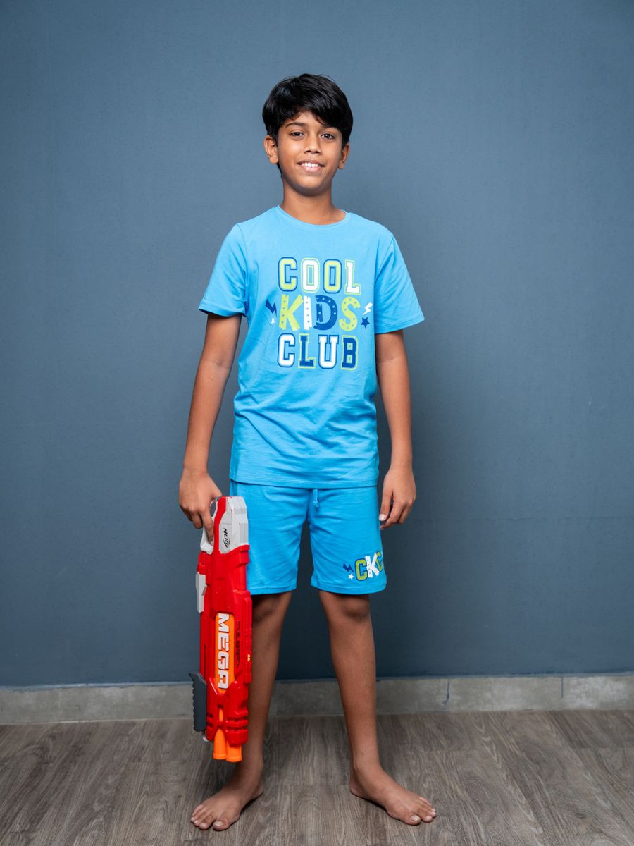 Child wearing a blue 'Cool Kids Club' t-shirt and shorts, holding a toy gun against a gray background