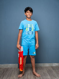 Child wearing a blue 'Cool Kids Club' t-shirt and shorts, holding a toy gun against a gray background