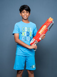 Child wearing a blue 'Cool Kids Club' shirt holding a red and white toy gun against a gray background