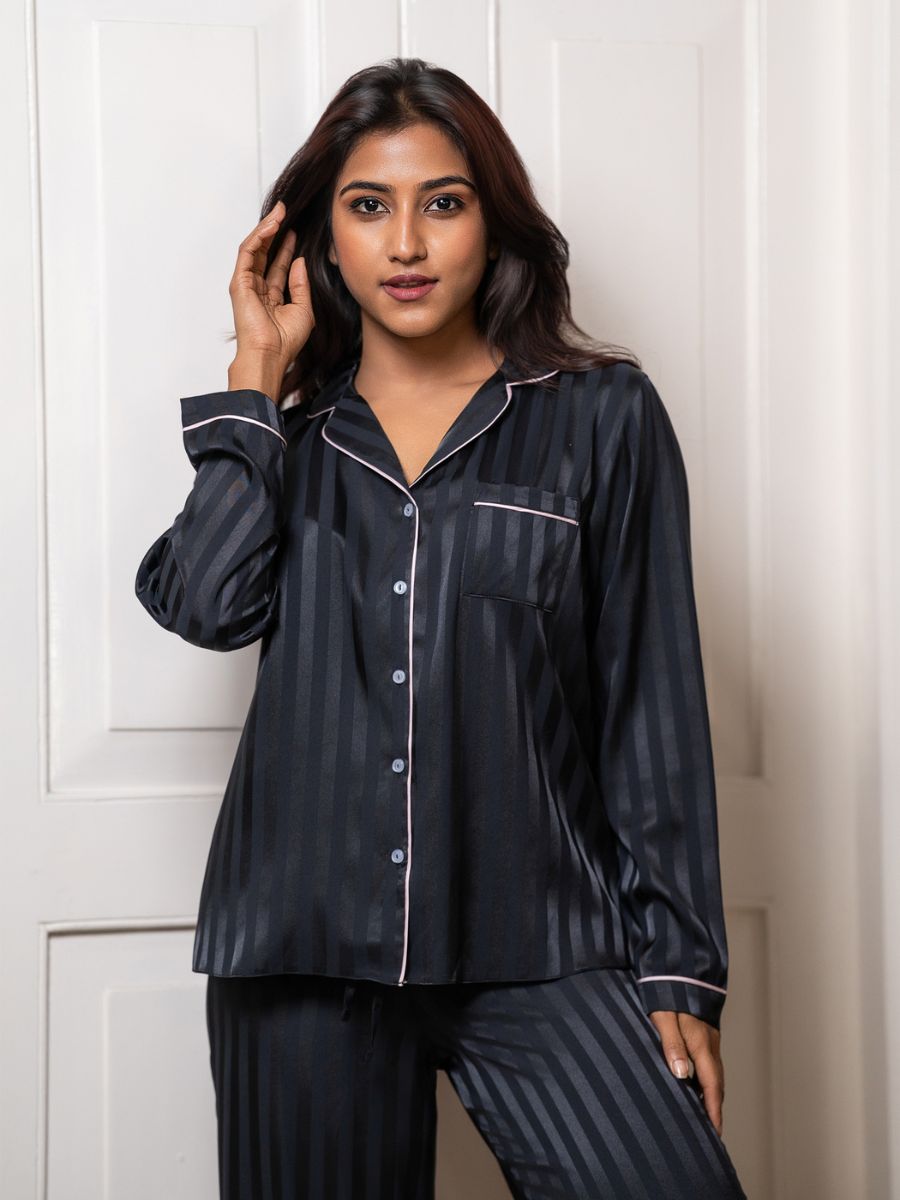 Woman wearing black satin pajamas with white piping against a white background