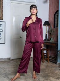 Woman wearing a burgundy satin pajama set in a room with a lamp and decor.