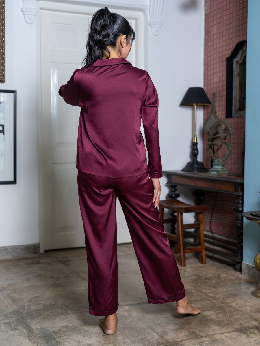 Person wearing burgundy satin pajamas standing in a room with a lamp and mirror.
