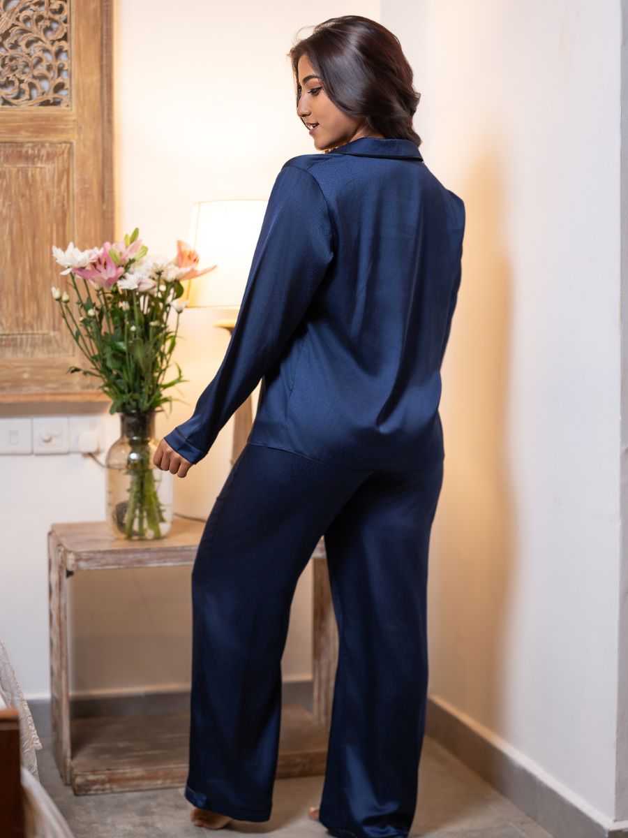 Woman in a navy blue outfit standing in a room with a vase of flowers on a table.