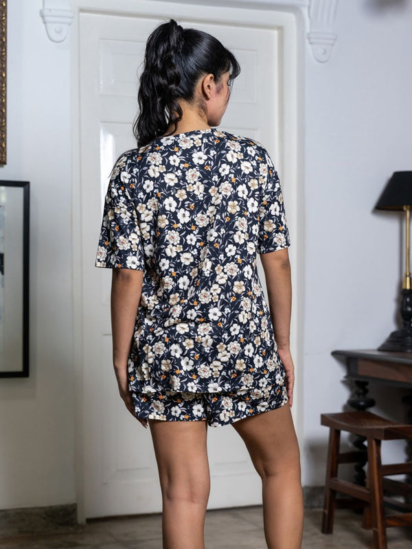 Person wearing a floral dress standing in a room with a white door and wooden furniture.