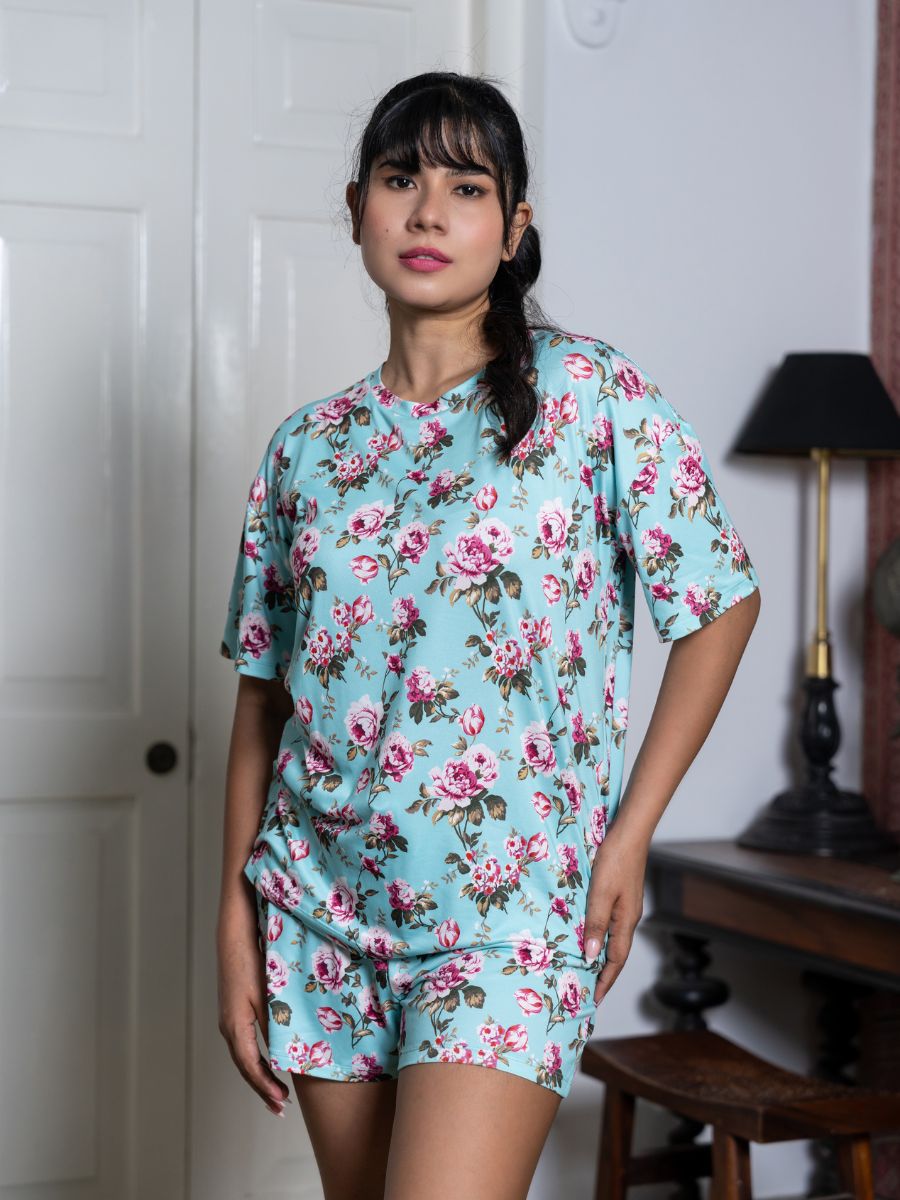 Woman wearing a floral pajama set in a room with a lamp and wooden table.
