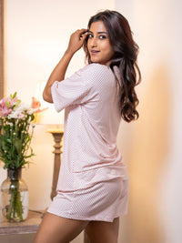Woman wearing a white polka dot outfit in a softly lit room with flowers in the background