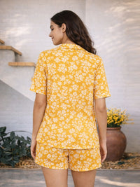 Woman wearing a yellow floral pajama set standing in a room with plants.