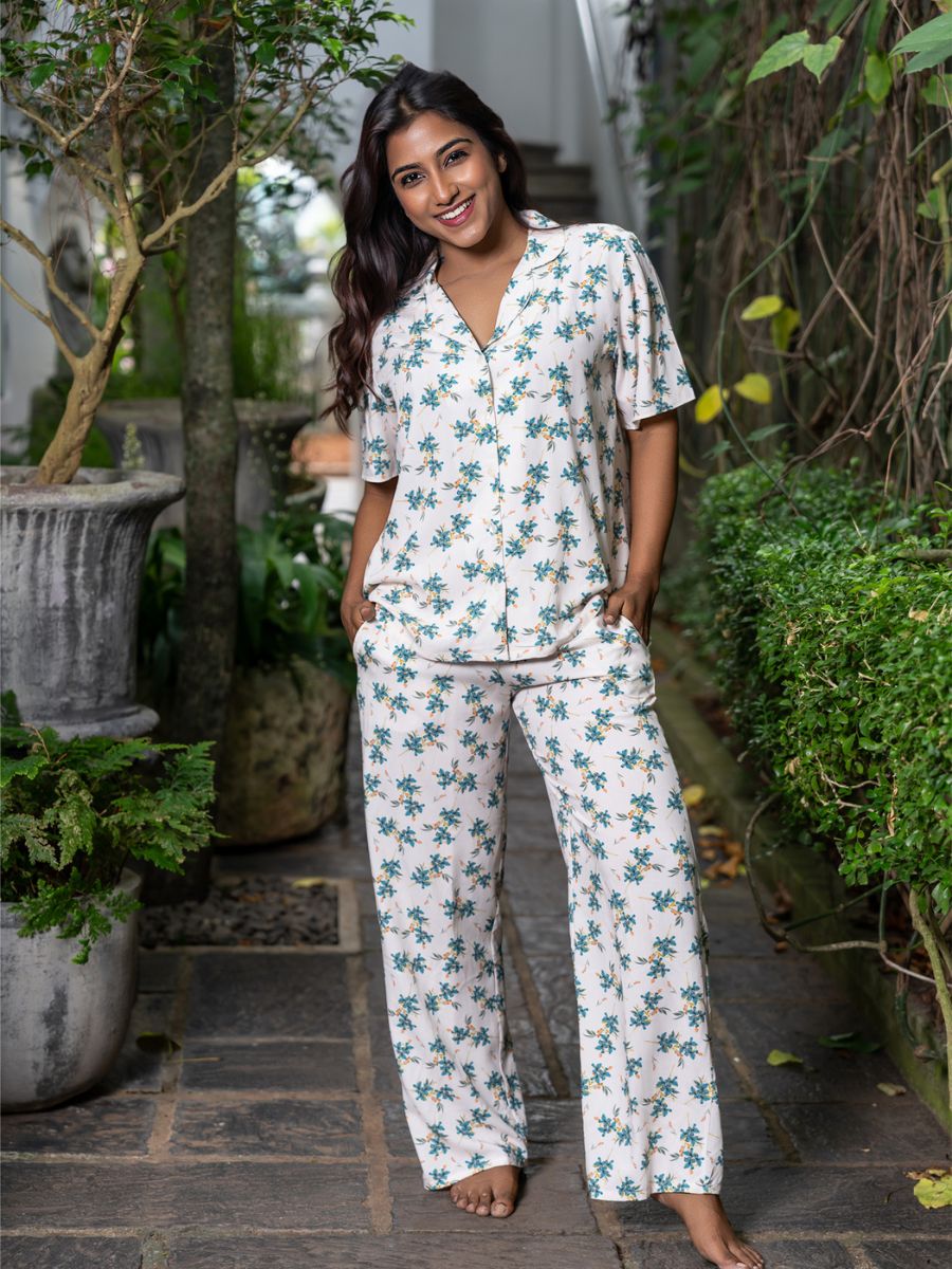 Woman wearing a floral pajama set standing outdoors with greenery around.
