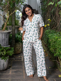 Woman wearing a floral pajama set standing outdoors with greenery around.