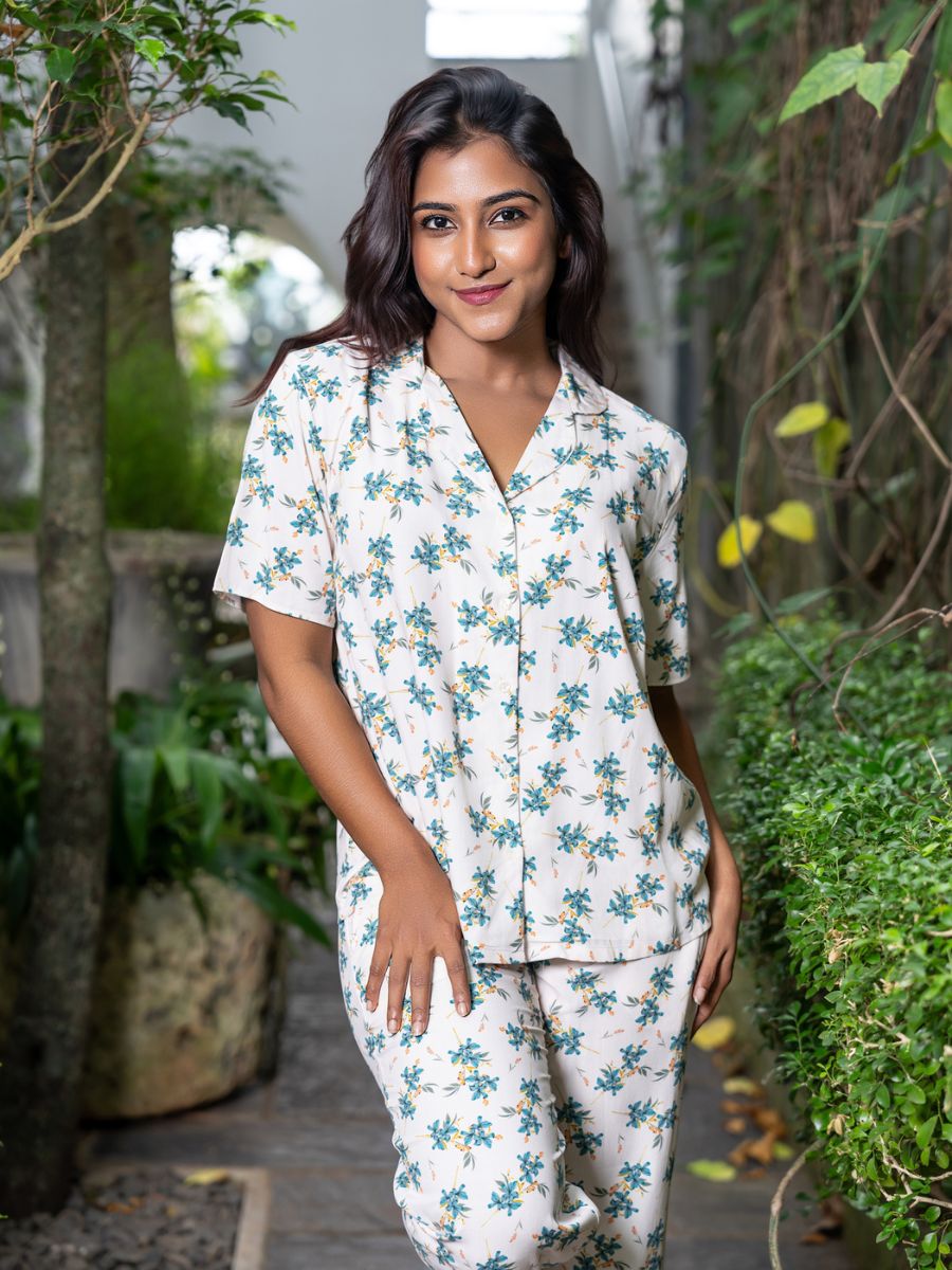 Woman wearing a white floral pajama set standing outdoors with greenery.