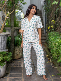 Woman wearing a floral pajama set standing outdoors with greenery around.