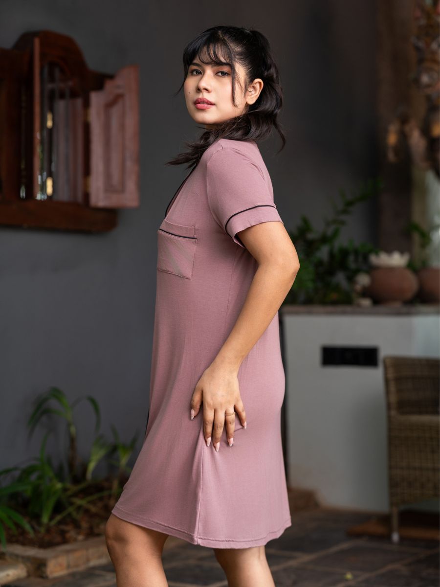 Woman wearing a pink dress standing in an indoor setting with plants and furniture.