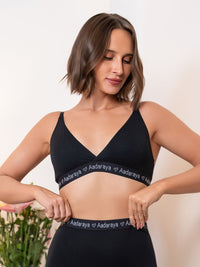 Woman wearing a black sports bra with 'Aadaraya' branding on a neutral background
