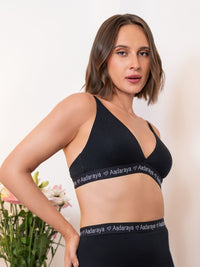 Woman wearing a black sports bra and leggings with 'Aadaraya' branding on a neutral background