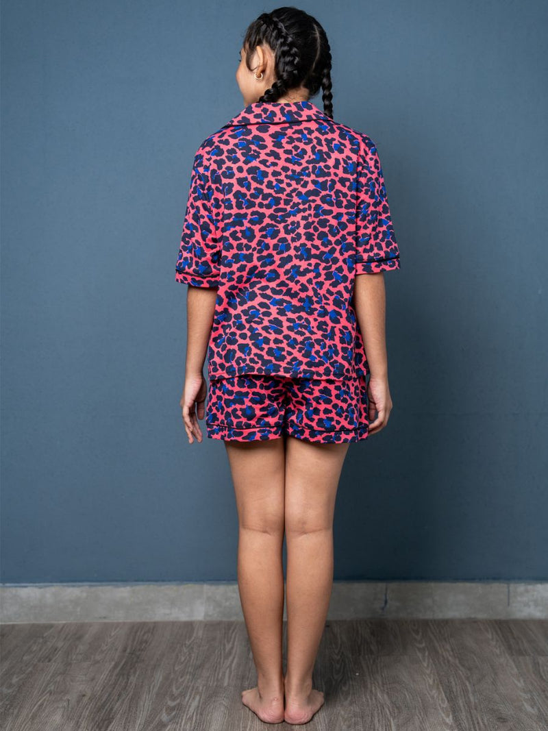 Person wearing a pink and blue leopard print outfit against a blue wall.