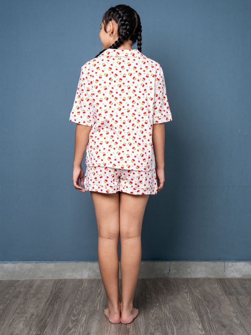 Person wearing a white shirt with red patterns and matching shorts against a blue wall.