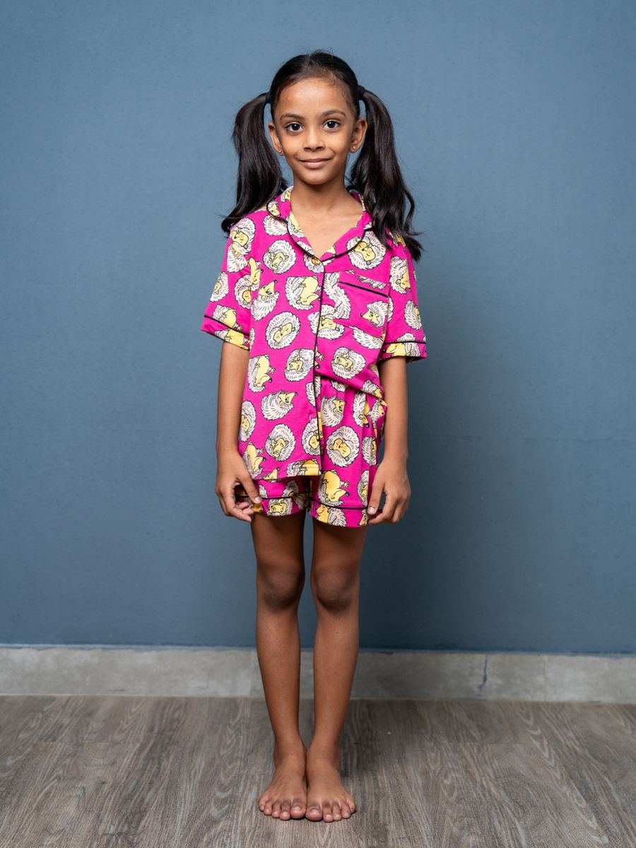 Young girl wearing a pink pajama set with cartoon characters against a blue wall.