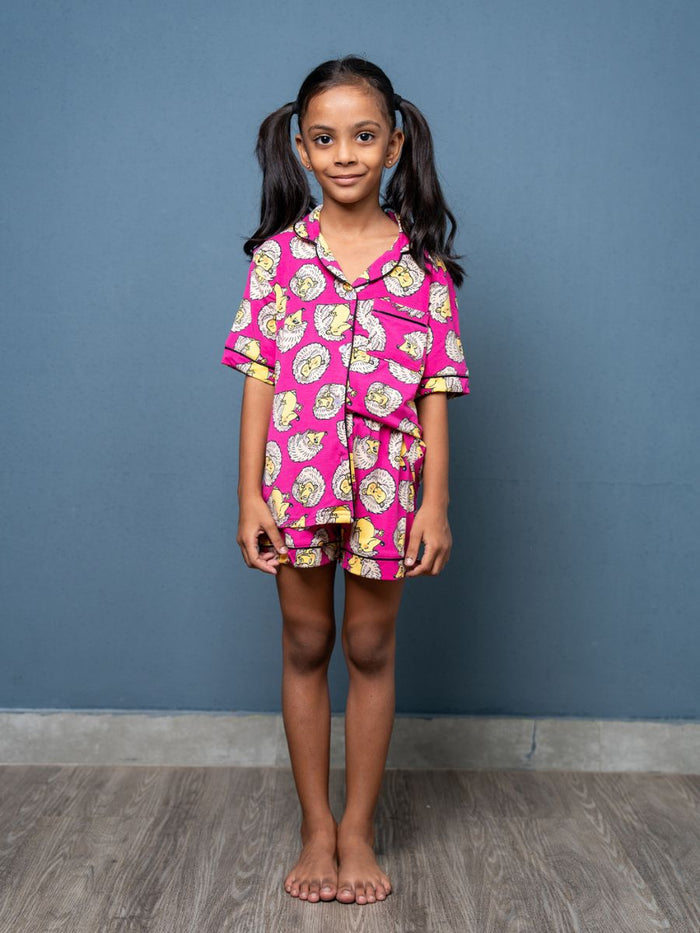 Young girl wearing a pink pajama set with cartoon characters against a blue wall.