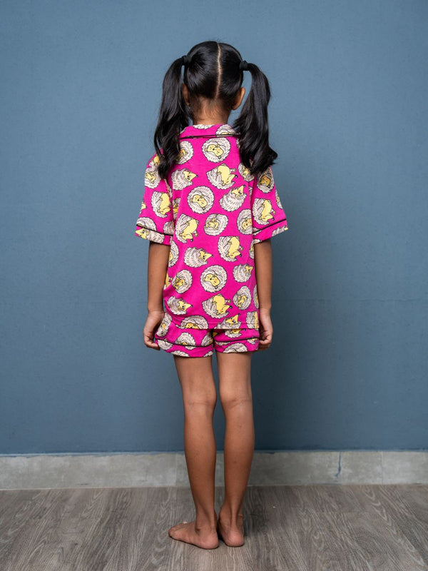 Child wearing a pink outfit with yellow patterns against a blue wall.