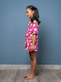 Child wearing a pink outfit with a floral pattern against a blue wall.