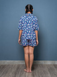 Person wearing a blue floral pajama set against a gray wall.