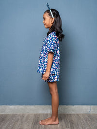 Child wearing a blue dotty dress against a gray wall