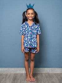 Young girl wearing a blue floral outfit with a crown against a gray background