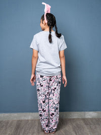 Person wearing a gray t-shirt and patterned pajama pants with bunny ears on a blue wall.