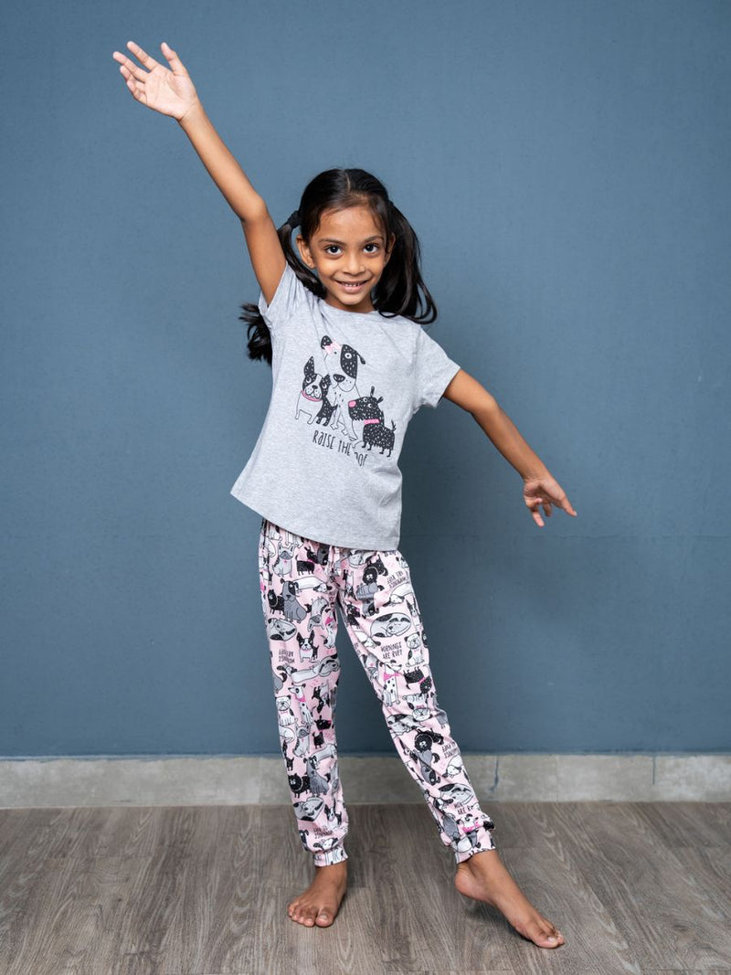 Child wearing a gray t-shirt with a design and patterned pants against a blue wall.