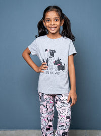 Young girl wearing a gray t-shirt with dog graphics and patterned pants against a blue background