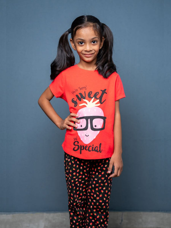 Young girl wearing a red t-shirt with a graphic design and black pants with pink hearts against a blue background