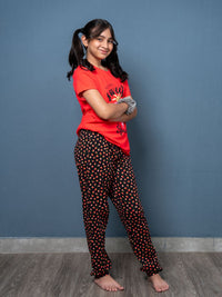 Girl wearing a red shirt and black polka dot pants against a blue wall.