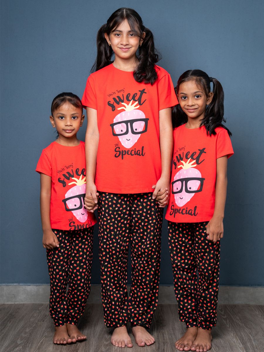 Three children wearing matching red shirts and black polka dot pants against a blue wall.