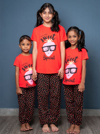 Three children wearing matching red shirts and black polka dot pants against a blue wall.