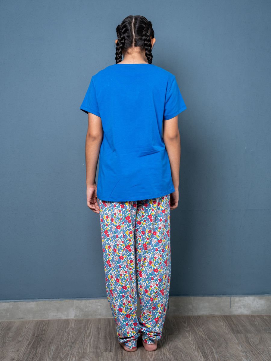 Person wearing a blue shirt and colorful patterned pants against a gray wall.