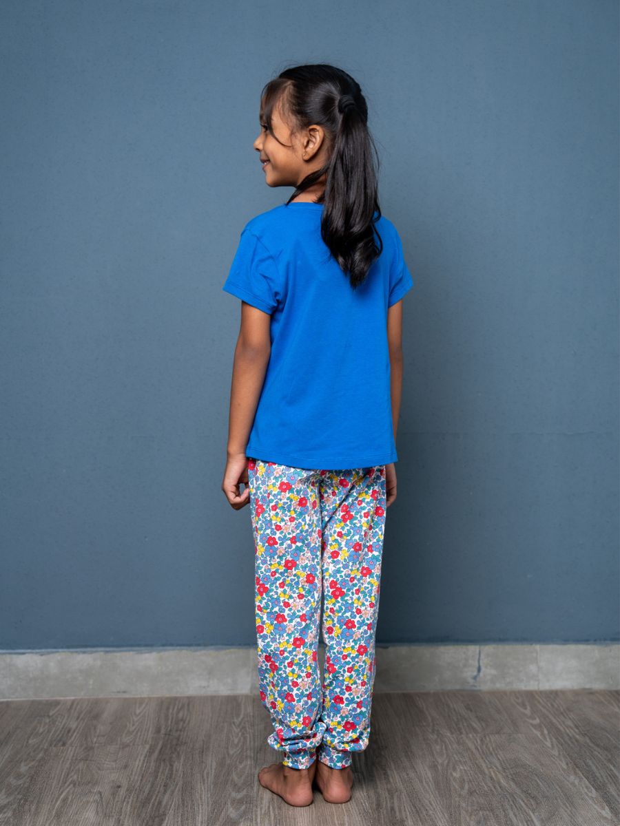 Child wearing a blue shirt and colorful floral pants against a gray wall.