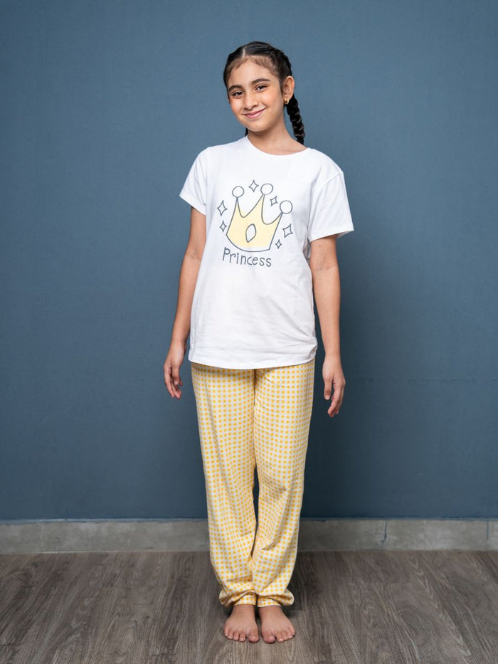Girl wearing a white t-shirt with a 'Princess' design and yellow checkered pants against a blue wall.
